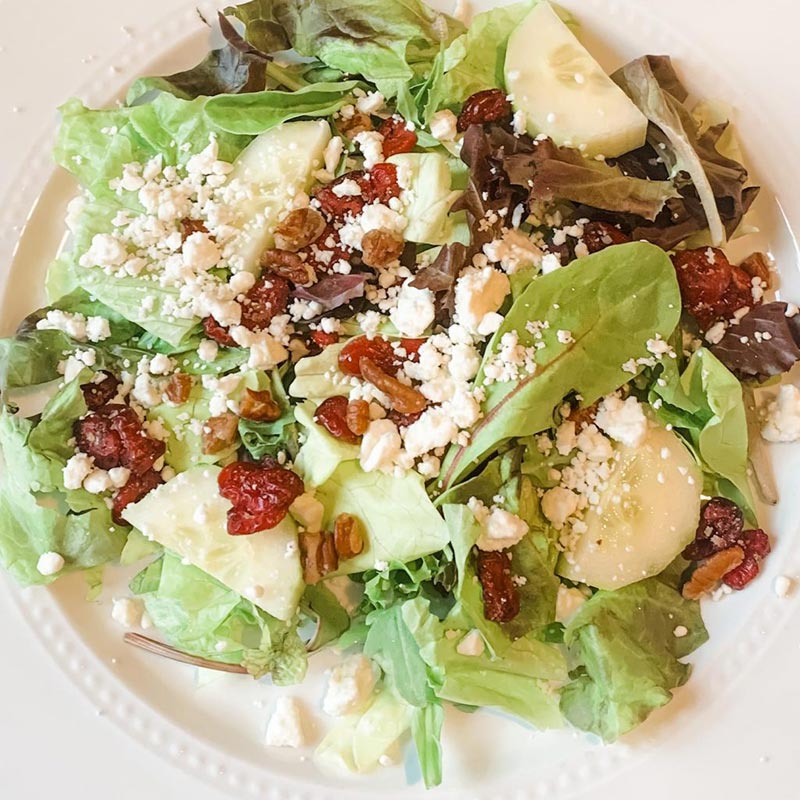 A salad with cranberries, pecans, veggies, and feta cheese.