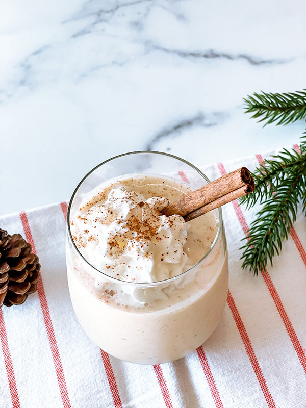 A glass of eggnog smoothie with sprinkled with cinnamon on top.