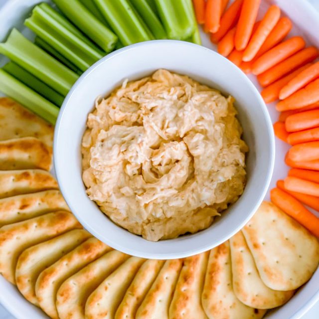 A tray of veggies and crackers with a bowl of buffalo chicken dip.