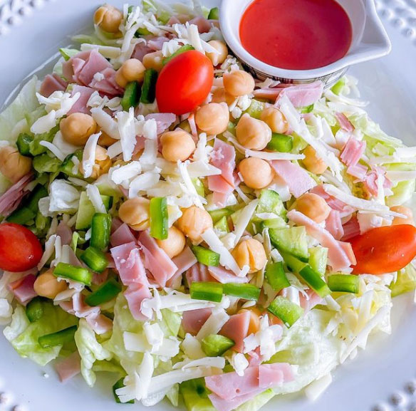 A salad with veggies, chickpeas, ham, and dressing on the side.