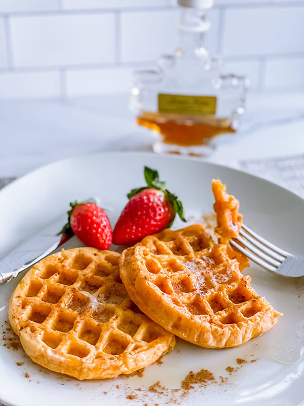 Sweet potato waffles on a plate with strawberries and syrup.