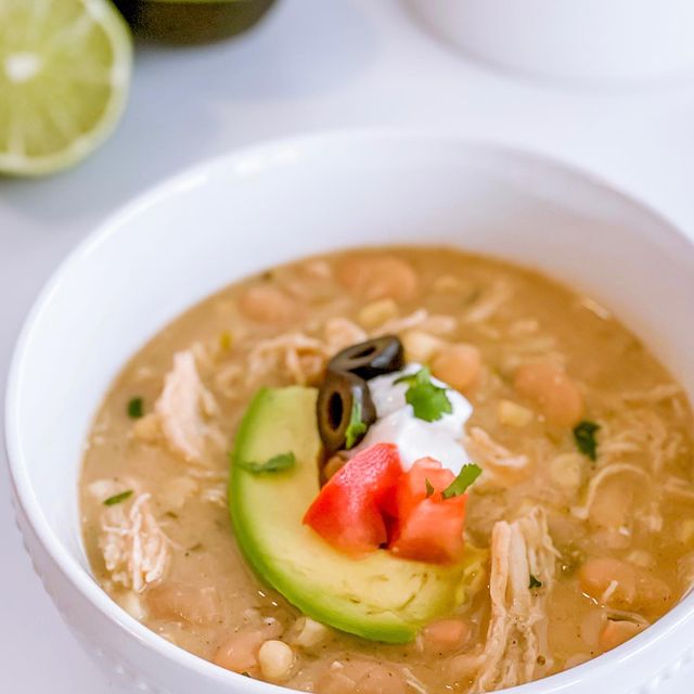 A bowl of white chicken chili with avocado and sour cream on top.