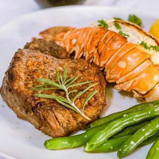 A steak and lobster served with a side of green beans.