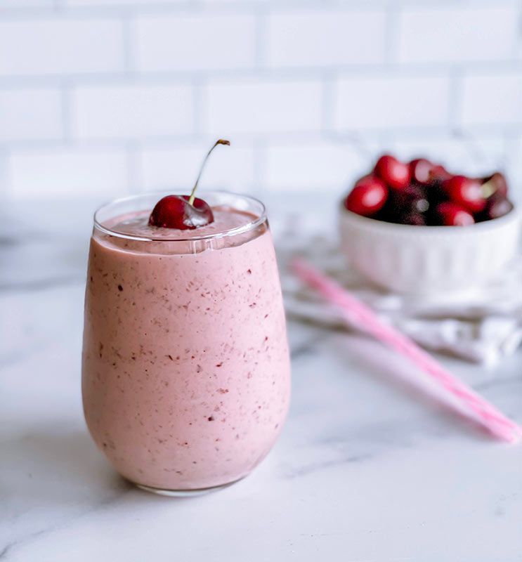 A glass of cherry vanilla smoothie with a fresh cherry on top.