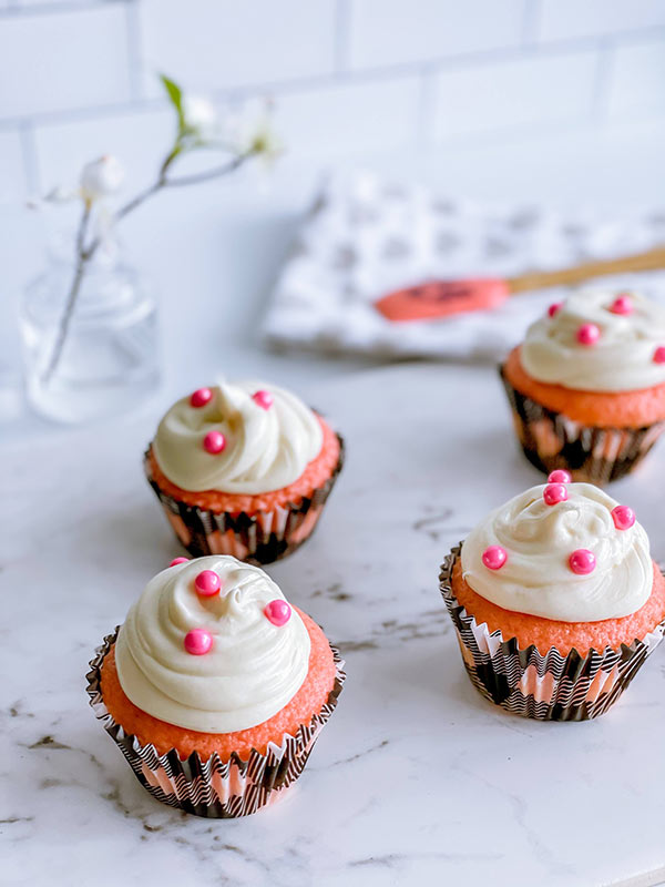 Pink velvet cupcakes with white frosting and pink sprinkles.