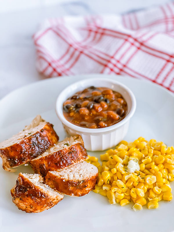 A plate of jerk chicken with a side of baked beans and corn.