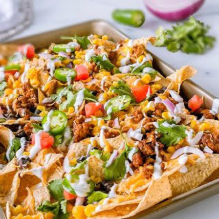 A baking sheet with layers of tortillas chips, meat, and vegetables.