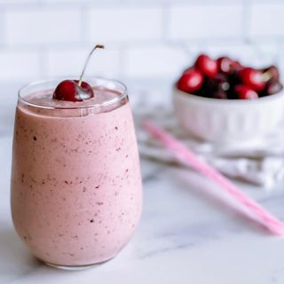 A cherry vanilla smoothie in a glass with a fresh cherry on top
