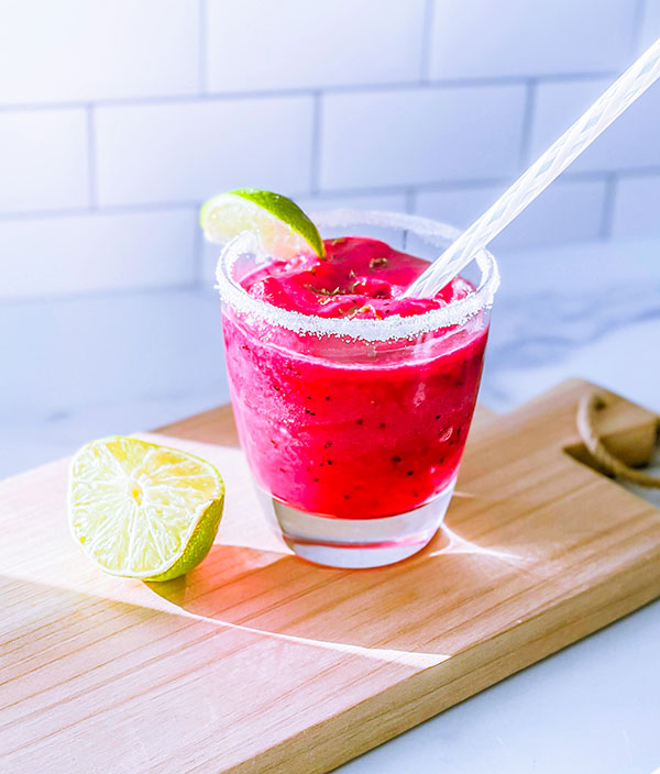 Bright pink dragon fruit smoothie in a glass with a lime wedge.