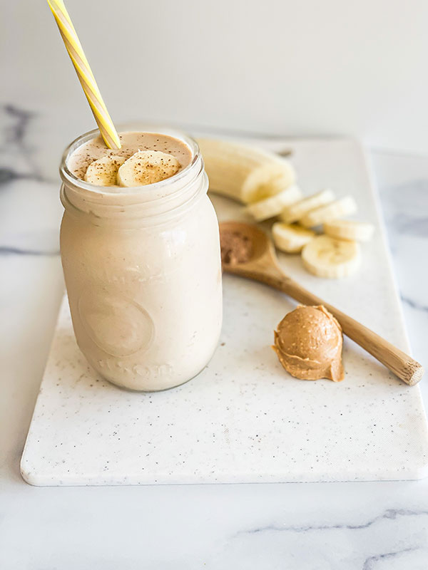 A peanut butter banana smoothie in a mason jar with a straw.