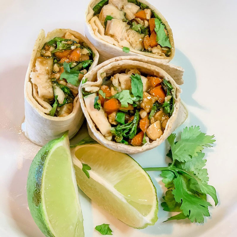 A plated peanut chicken wrap served with lime wedges.