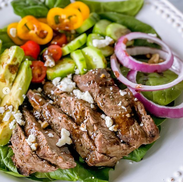 A closeup of steak salad on a plate with veggies and dressing.