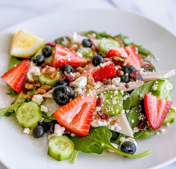 A colorful salad with berries, veggies, nuts, and feta cheese.